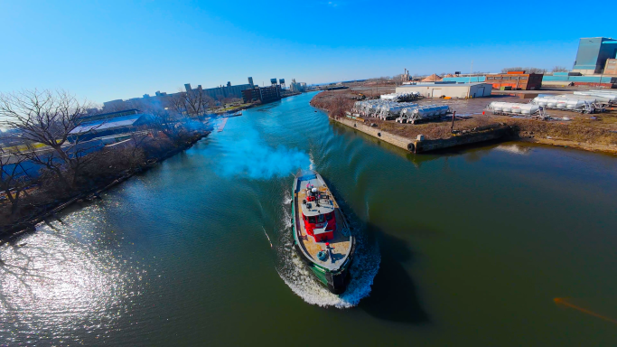A boat navigates through a calm river with buildings along the banks under a clear blue sky.