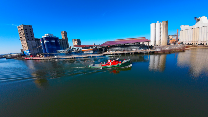 A small boat on a calm river near urban buildings under a clear blue sky.