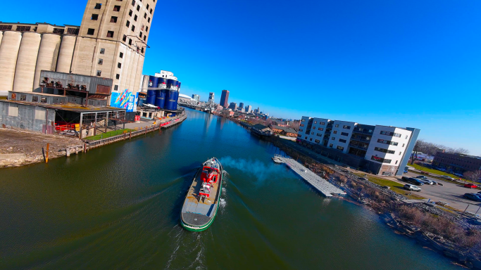 A boat navigates a calm waterway with buildings lining the shore under a clear blue sky.